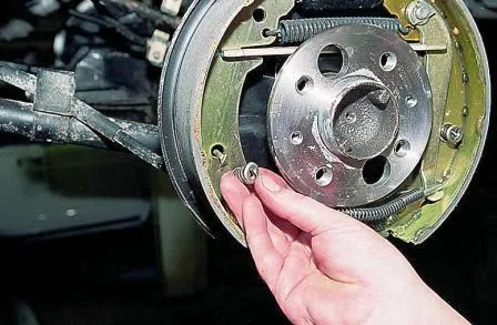 Нажимаем на чашку опорной стойки колодки и, повернув на 90°, снимаем ее и пружину